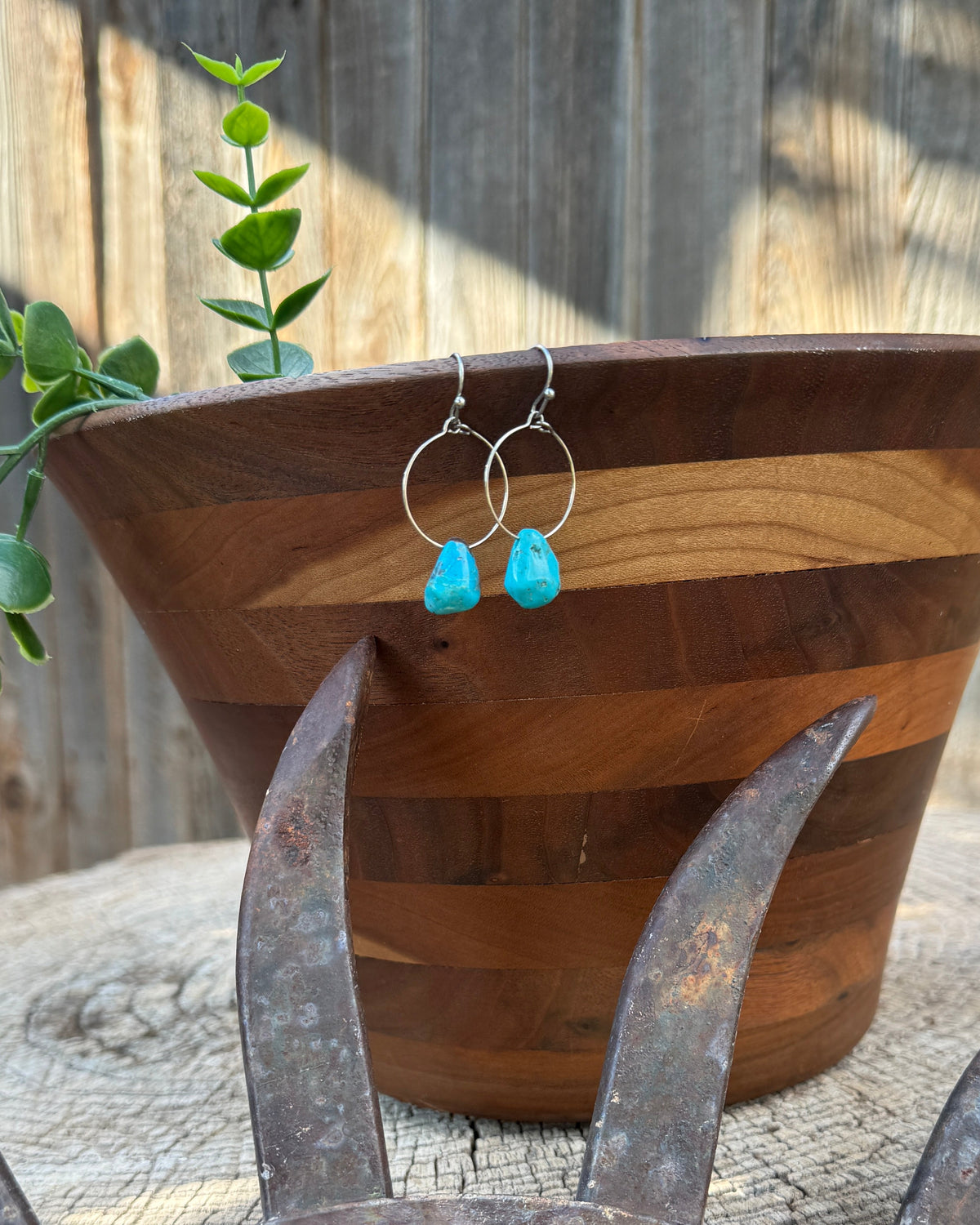 Tie-on hoop earrings with bright turquoise blue teardrop beads and silver wire hoops, displayed on a wooden planter in an outdoor rustic setting.